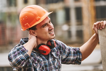 Be careful. Construction worker in protective helmet feeling neck pain while working at construction...
