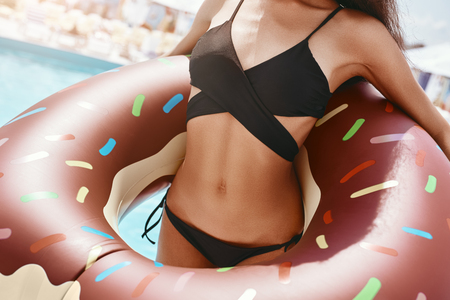 Close up of a woman wearing black swimsuit and holding inflatable swim ring in shape of donutの写真素材
