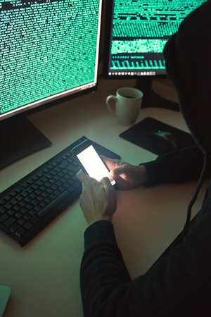 Personal information. Vertical photo of young hacker in black hoodie using multiple computers and...