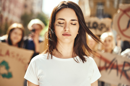 Changing the world. Young and brave woman with word freedom written on her face and with closed eyes standing around female activists on the road during protest marchの写真素材