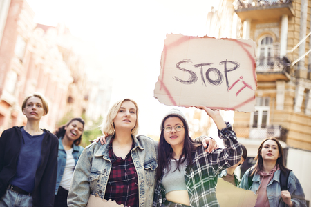 Stop violence against women. Two young women are holding a banner with word stop it while standing on the road during a womens march in front of female activists.の写真素材