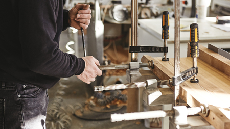Craftsman using clamps fixate two pieces of wood and iron. The process of making desk, furniture....