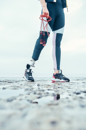 Ready to jump. Cropped image of young woman with prosthetic legin sports clothing holding skipping...