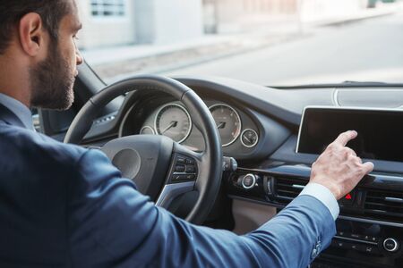 Modern businessman. Side view of young bearded businessman in formal wear is touching control panel while driving his new car.の写真素材