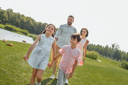 Happy kids. Young family of four holding hands, smiling and walking outdoors near the riverの写真素材