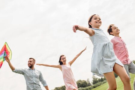 Summertime. Happy and young family of four launcinging a kite in the field.の写真素材