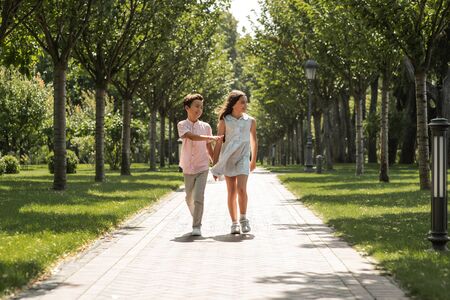 You are my best frind. Little boy and girl holding hands and smiling while walking together in parkの写真素材