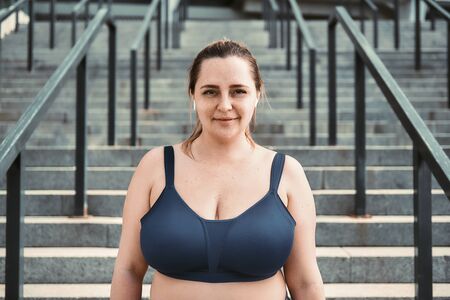 Portrait of cheerful plus size woman in sporty top standing on stairs and looking with smile at camera.の写真素材