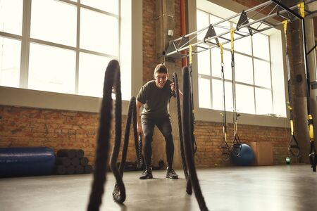 Battle ropes exercises. Young and strong man doing CrossFit exercises with a rope at gym