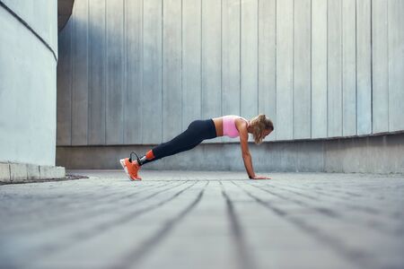 Strong body. Full-length of young woman with leg prosthesis in sportswear doing plank exercise...
