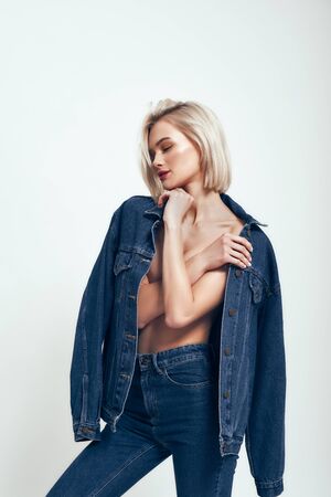 Great look. Sexy young woman in jeans wear keeping eyes closed while standing against grey background in studio. Denim clothes. Fashion concept. Beautyの写真素材