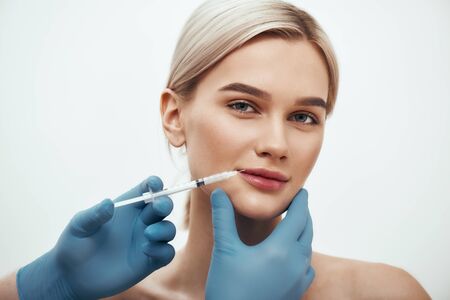 Cosmetic injection. Young beautiful woman looking at camera and smiling while doctors hand making an...