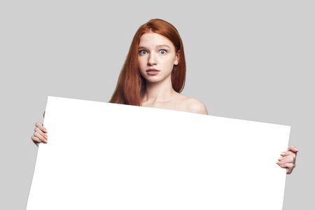 Your text here. Beautiful and young redhead woman holding empty blank board and looking at camera...