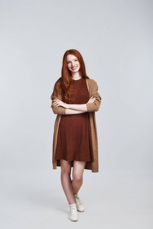 Simply happy Full-length photo of cheerful and cute young redhead lady in casual clothing smiling and looking at camera while standing against grey backgroundの写真素材