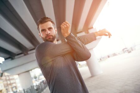 Did you workout today Portrait of young bearded man in sportswear stretching his arm while standing...