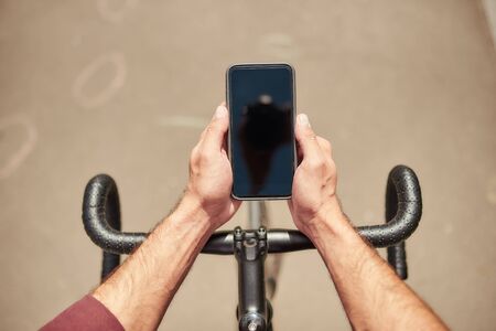 Top view of man riding his bicycle and looking at his mobile phone while standing outdoors