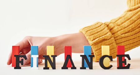 Finance word created with alphabet letters. Hand placing multi-colored wooden blocks in the backgroundの写真素材
