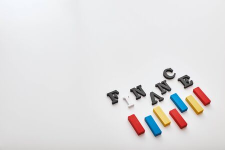 Finance word created with cubes alphabet letters near multi-colored wooden blocks lying diagonally