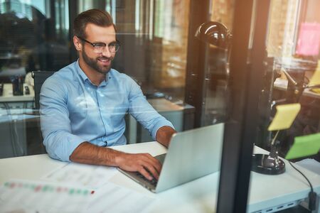 Great results Young bearded businessman in eyeglasses and formal wear looking at laptop and smiling...