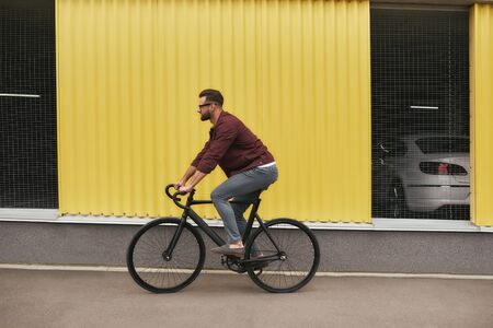 On the way. Side view of handsome man with stubble in casual clothes riding on his bicycle