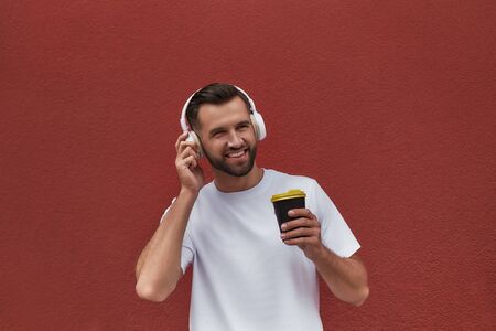 Enjoying this day Portrait of happy handsome man in headphones listening to the music and drinking...