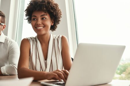 Successful project. Young and beautiful afro american woman working on laptop and looking away with...