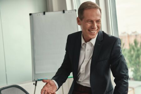 Happy businessman. Handsome and cheerful mature man in formal wear looking away and smiling while sitting in the officeの写真素材