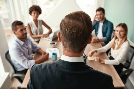 Back view of business man in formal wear discussing something with his colleagues while having a meeting in the officeの写真素材