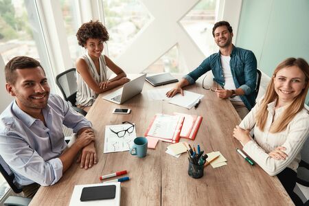 Strong team. Group of young business people looking at camera and smiling while working together in the modern officeの写真素材