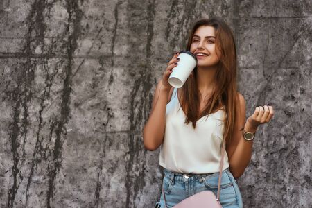 Beautiful stylishly dressed girl posing over concrete background