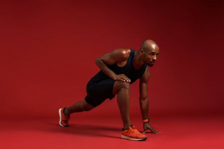 Warming up before training. Young and strong african man in sports clothing stretching while...