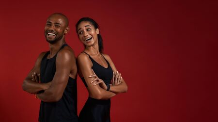 Staying healthy. Young and positive african fitness couple in sportswear looking at camera with smile while standing against red backgroundの写真素材