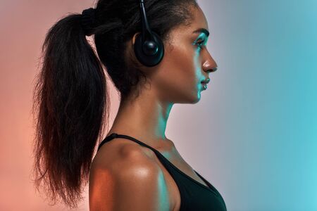 My favourite song. Side view of attractive young athlete woman in headphones standing against colorful backgroundの写真素材