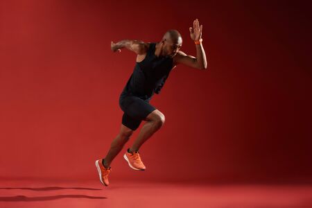 Never give up. Full length of young african man in sports clothing running in studio against red backgroundの写真素材