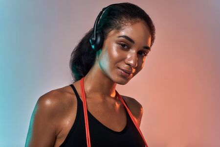 Exercising with music. Portrait of beautiful young woman in headphones holding jumping rope on...