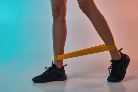 Cropped photo of woman doing exercises with resistance band while standing in studio against colorful backgroundの写真素材
