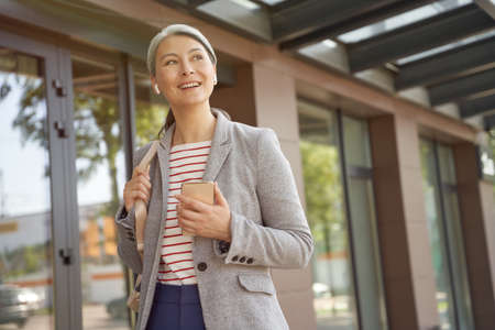 Portrait of a beautiful and happy woman wearing wireless earphones using smartphone, talking with...