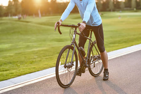 Getting ready to ride. Cropped shot of a road bicycle racer in sportswear standing on the road in park at sunset, cycling outdoorsの写真素材