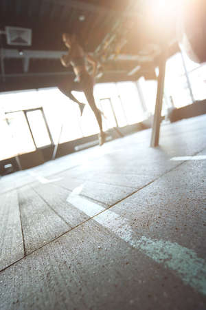 Sport training concept. Vertical shot of athletic woman in sportswear working out at industrial gym, focus on the floorの写真素材