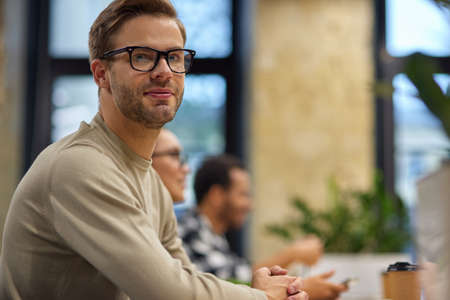 Young handsome man, male office worker sitting at desk in the board room and looking at camera while...