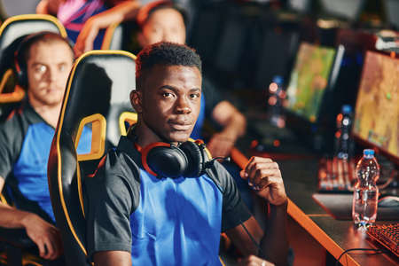 Professional cybersport gamer looking at camera with serious facial expression, participating with...