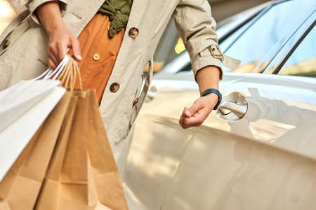 Cropped shot of a woman holding shopping bags and opening her car with smartwatch while standing on the city streetの写真素材