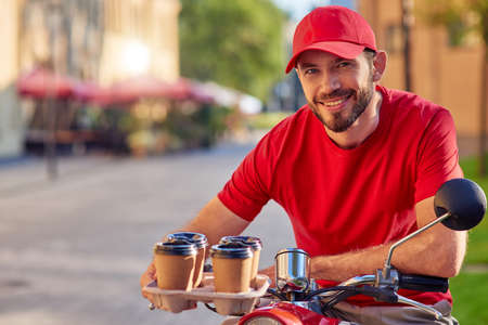 Young caucasian male courier delivering coffee on scooterの写真素材