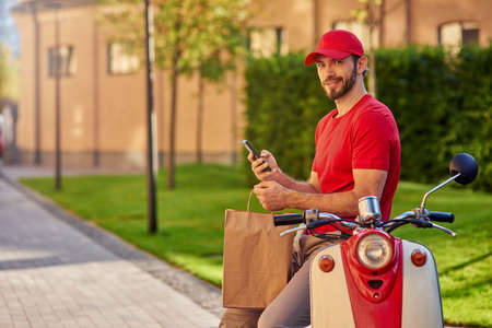 Young cheerful caucasian man courier delivering paper packetの写真素材