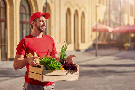 Young cheerful caucasian male courier delivering groceryの写真素材
