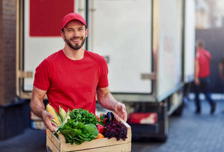 Young cheerful caucasian male courier holding grocery in boxの写真素材