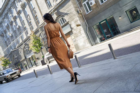 Full length of a young fashionable woman wearing long romantic dress and high heel shoes walking on the city streets, rear viewの写真素材