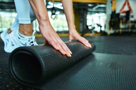 Cropped shot of a fitness woman in sportswear rolling yoga mat while working out at gym