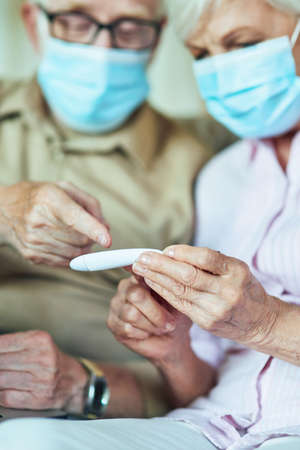 Senior man in a mask pointing with a finger at a thermometer