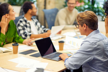 Teamwork. Group of young multiracial people sitting at the table in board room in the modern office, using modern technologies and working on project togetherの写真素材